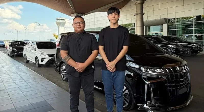 Alpha Car Rental staff standing with a Toyota Alphard at Kuching International Airport (KIA) pickup point.